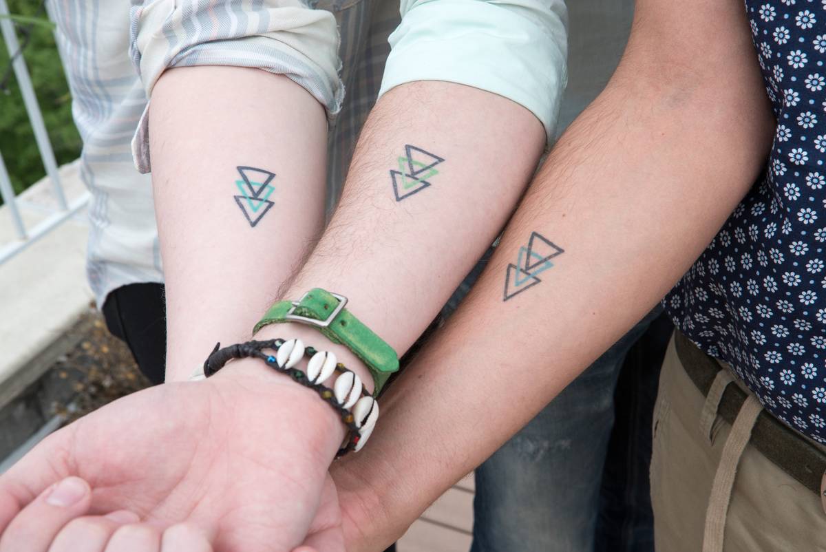 Three people have matching tattoos on their forearms.