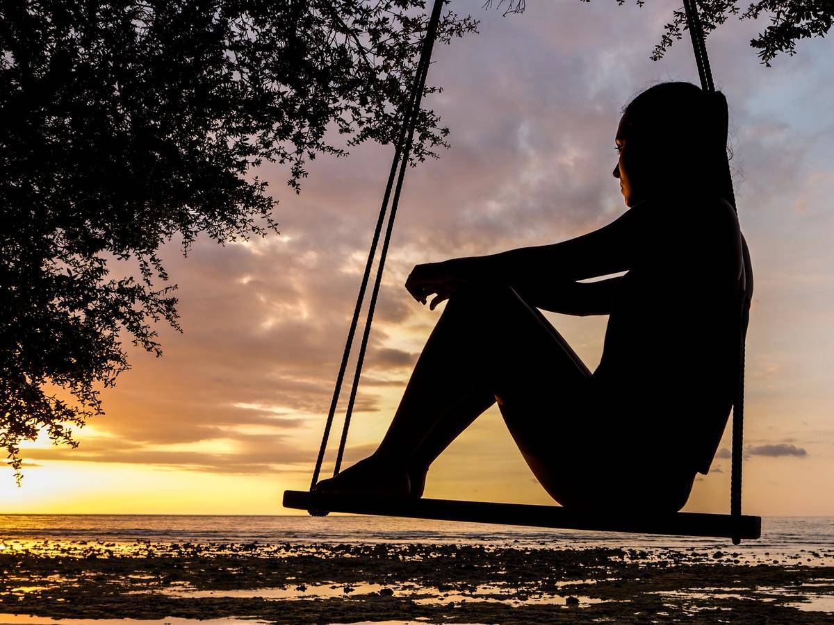 a woman sitting on a swing looking out at a beach 