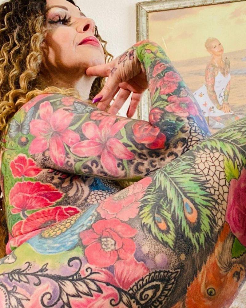 Close-up shot of woman's thigh tattoos, she poses with a hand under chin. Only her face and neck have no tattoos 