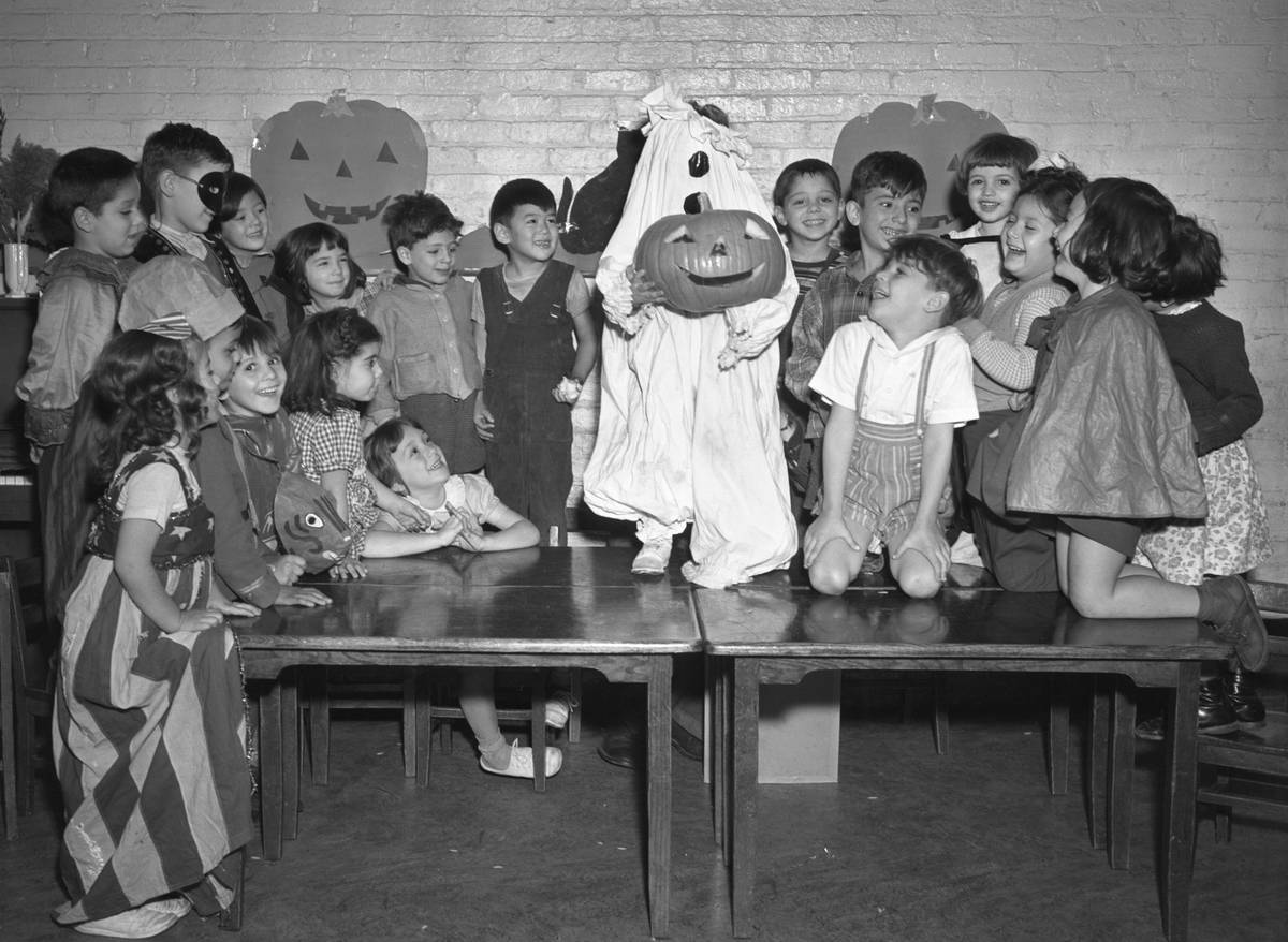 Children at school on Halloween with one student dressed up as a pumpkin ghost standing in the middle