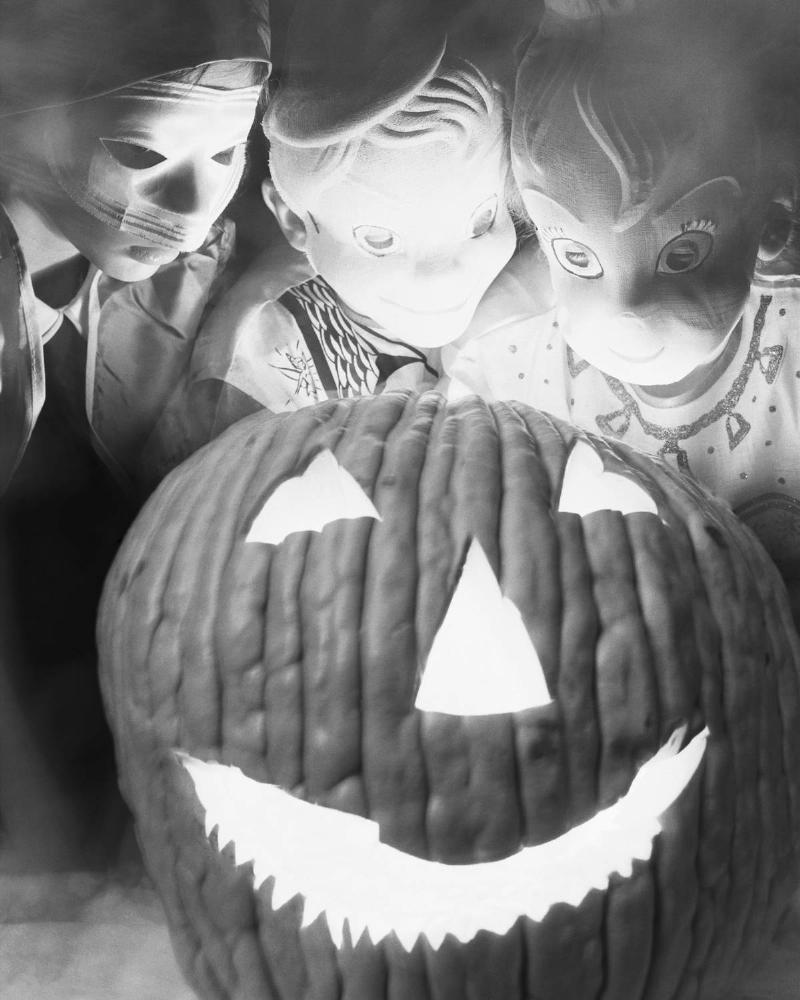 Children dressed as goblins surround a jack-o'-lantern in a photo from 1953