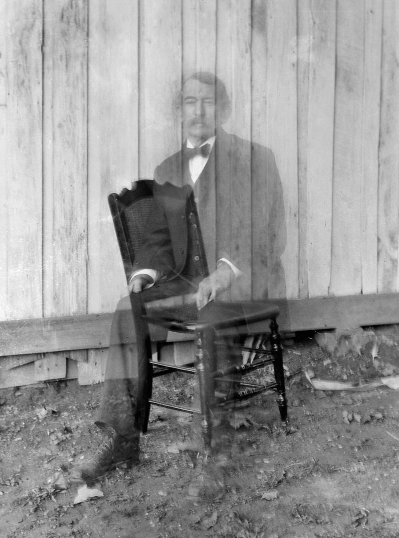 Double exposure of a man sitting on a chair making it look like he's a ghost from 1900