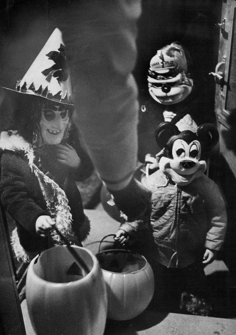 A small group of children wear costumes and masks and walk house to house trick-or-treating on Halloween