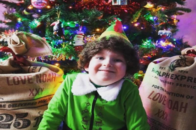 noah dressed as an elf with a christmas tree and presents