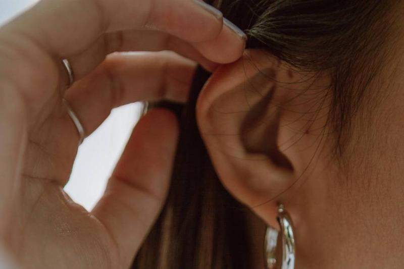 A woman touching her ear, with an earring dangling.