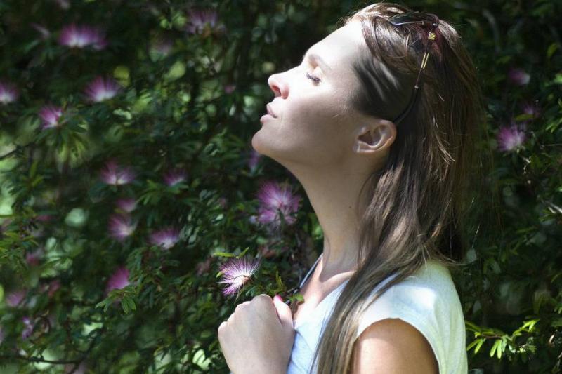 A young woman taking a deep breath outside.