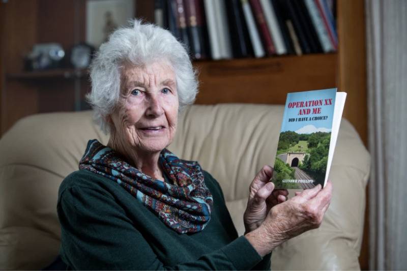 Mrs Phillips has published her husband's life story into a book, titled 'Operation XX And Me: Did I Have A Choice?'  posing holding it