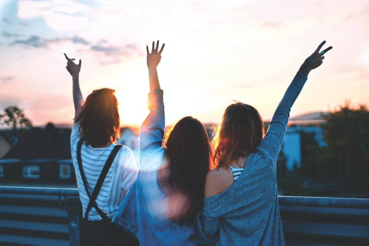 Three Girls with their hands up facing the sunset