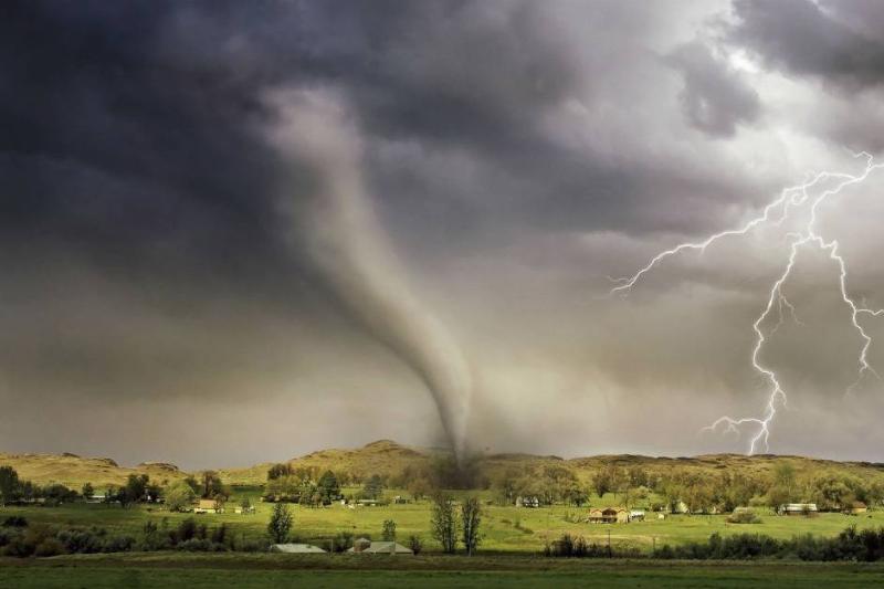 A tornado hits the ground with a dark sky and lightning bolts.
