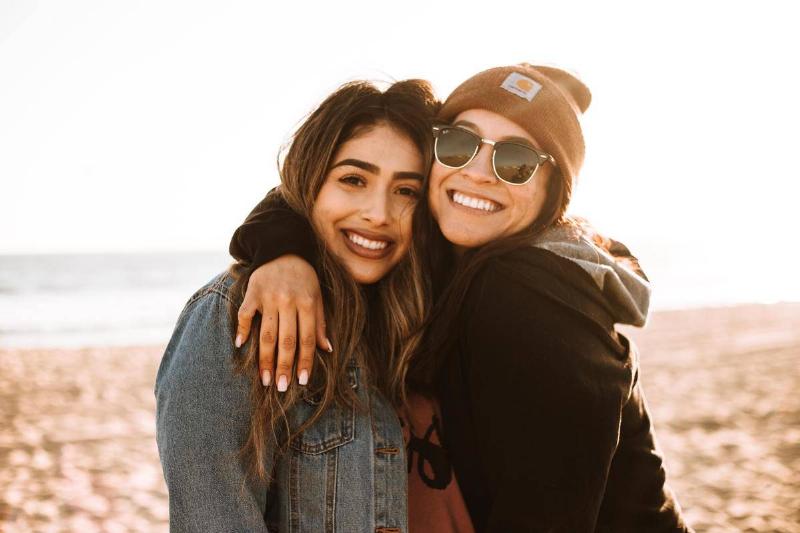 Two young adult women smiling and hugging.