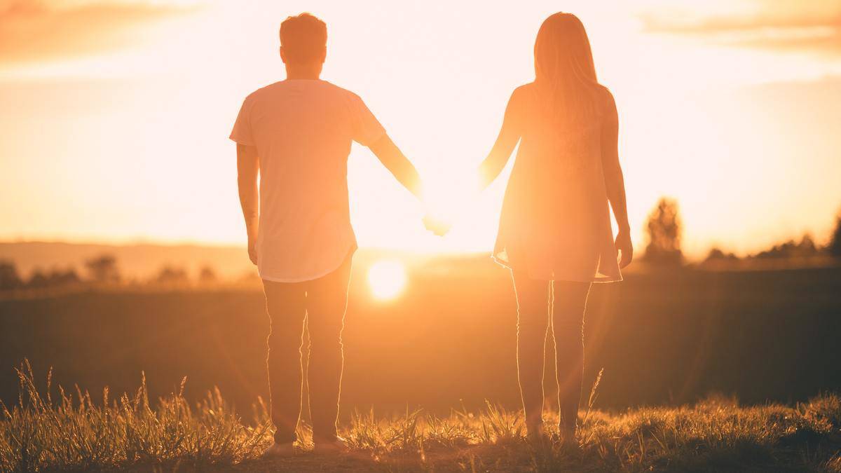 man and woman holding hands by sunset in a field