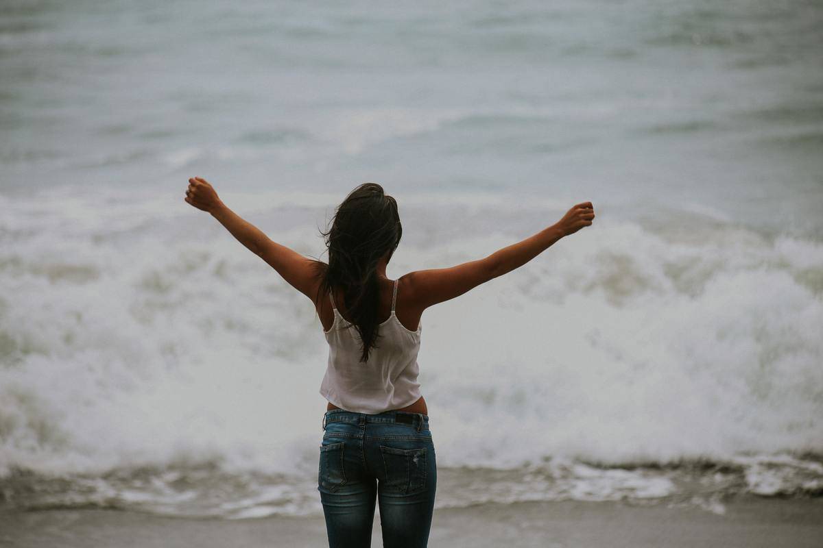 woman with arms raised in triumph while facing ocean