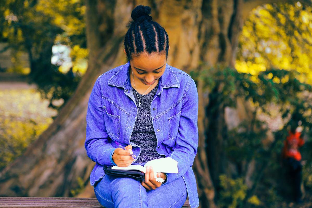 woman sitting on a bench while writing in journal