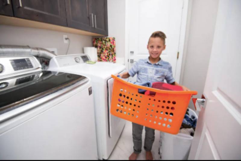 young boy carries laundry basket in laundry room