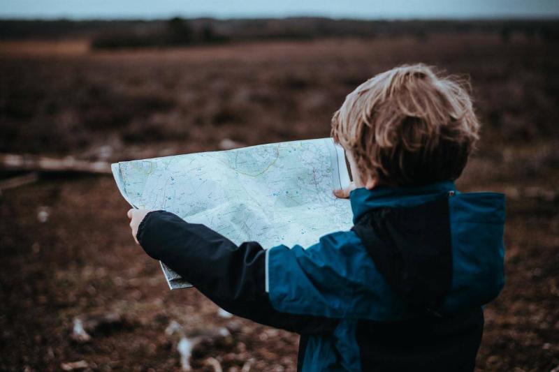 A small boy from behind, looking at a map and standing in a field.