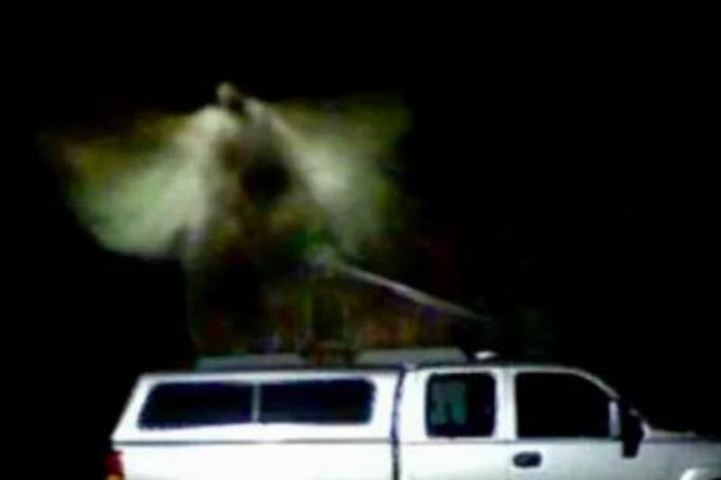 A blurry figure on top of a white truck that looks like an angel
