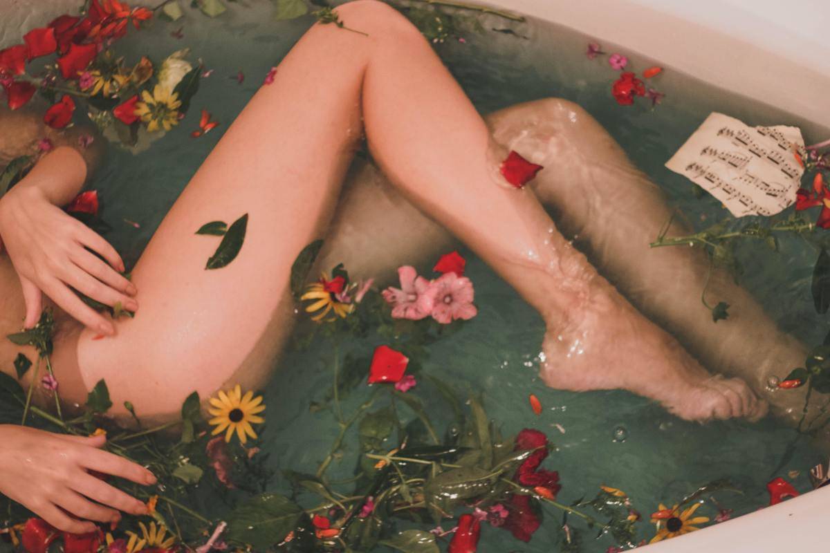A woman's legs in a bath with flower petals.