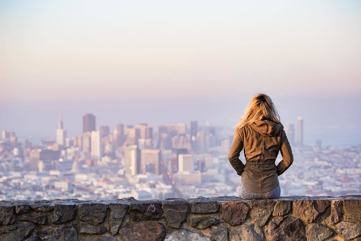 A woman sitting on a stone bench overlooking a city in the distance.