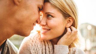 couple sit forehead to forehead while gazing into each other's eyes and smiling with the sunlight peaking through their faces