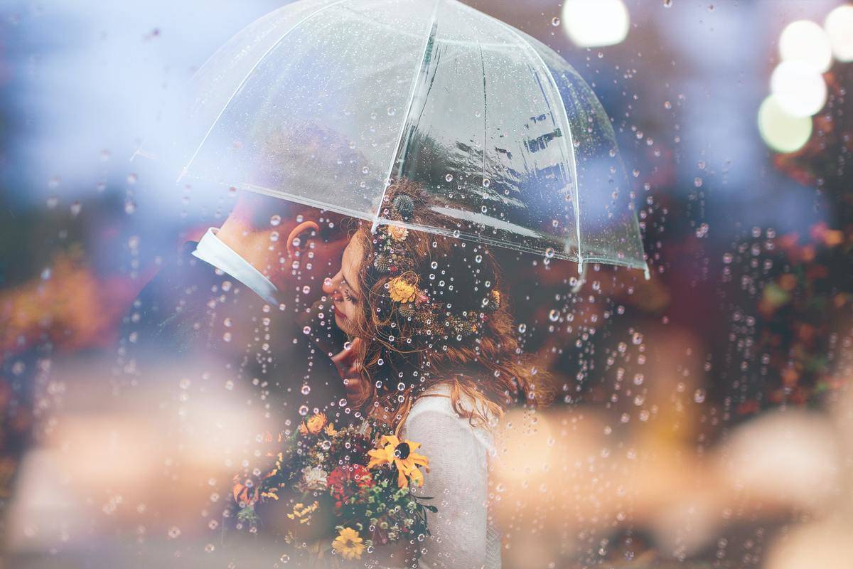 Couple stands under umbrella in the rain embracing