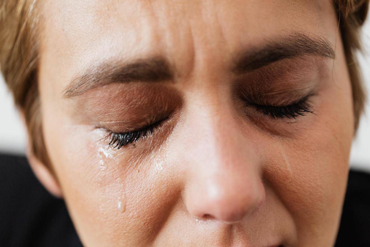A close-up of a woman's face with closed eyes and tears rolling down her cheeks.