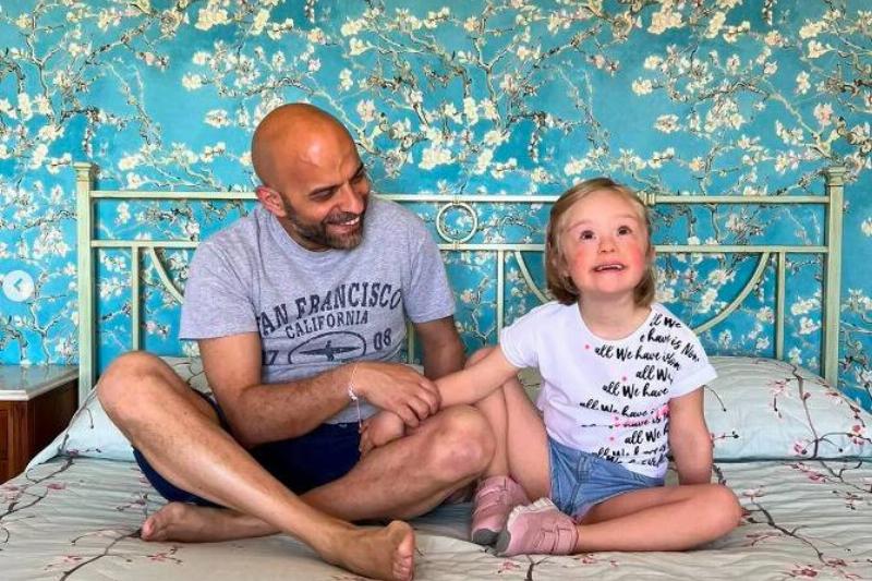 A daughter and father sitting on a bed smiling.
