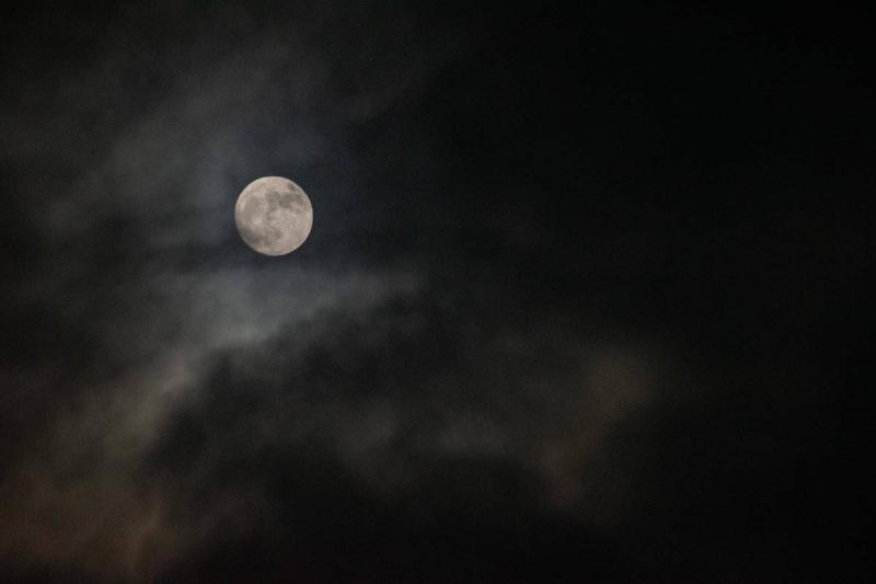 A full moon hanging in a dark, cloudy sky.