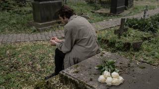 A man sitting in a graveyard, with white flowers behind him.