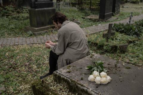 A man sitting in a graveyard, with white flowers behind him.