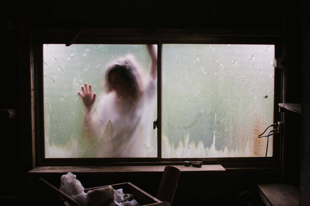 A blurry figure of a woman pressed against a foggy window.