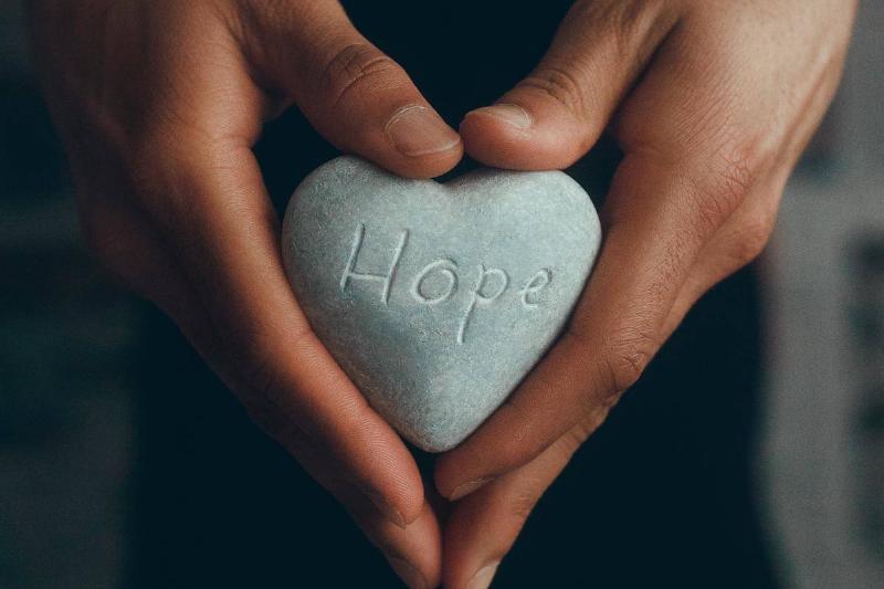Hands holding a heart-shaped rock with the word hope engraved on it.