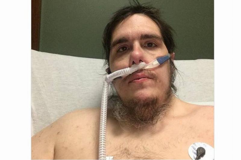 A man sitting on a hospital bed, taking a selfie with tubes in his nose.