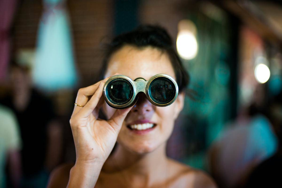 A woman looking through binoculars, a blurred background.