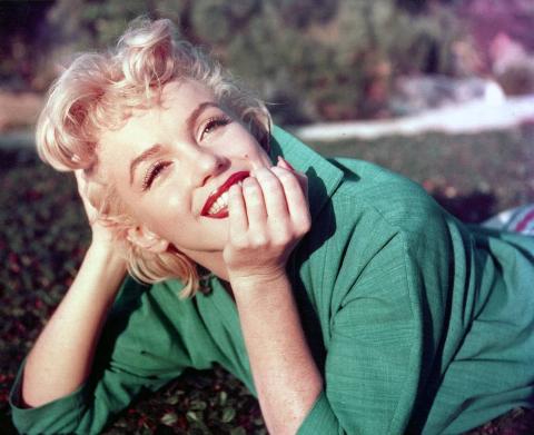 Marilyn Monroe in a green shirt smiling on the grass.