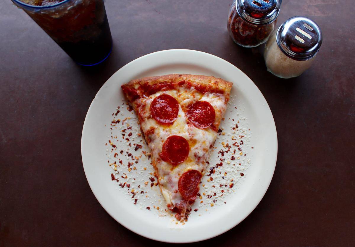 A slice of pepperoni pizza on a white plate next to salt and pepper shakers.