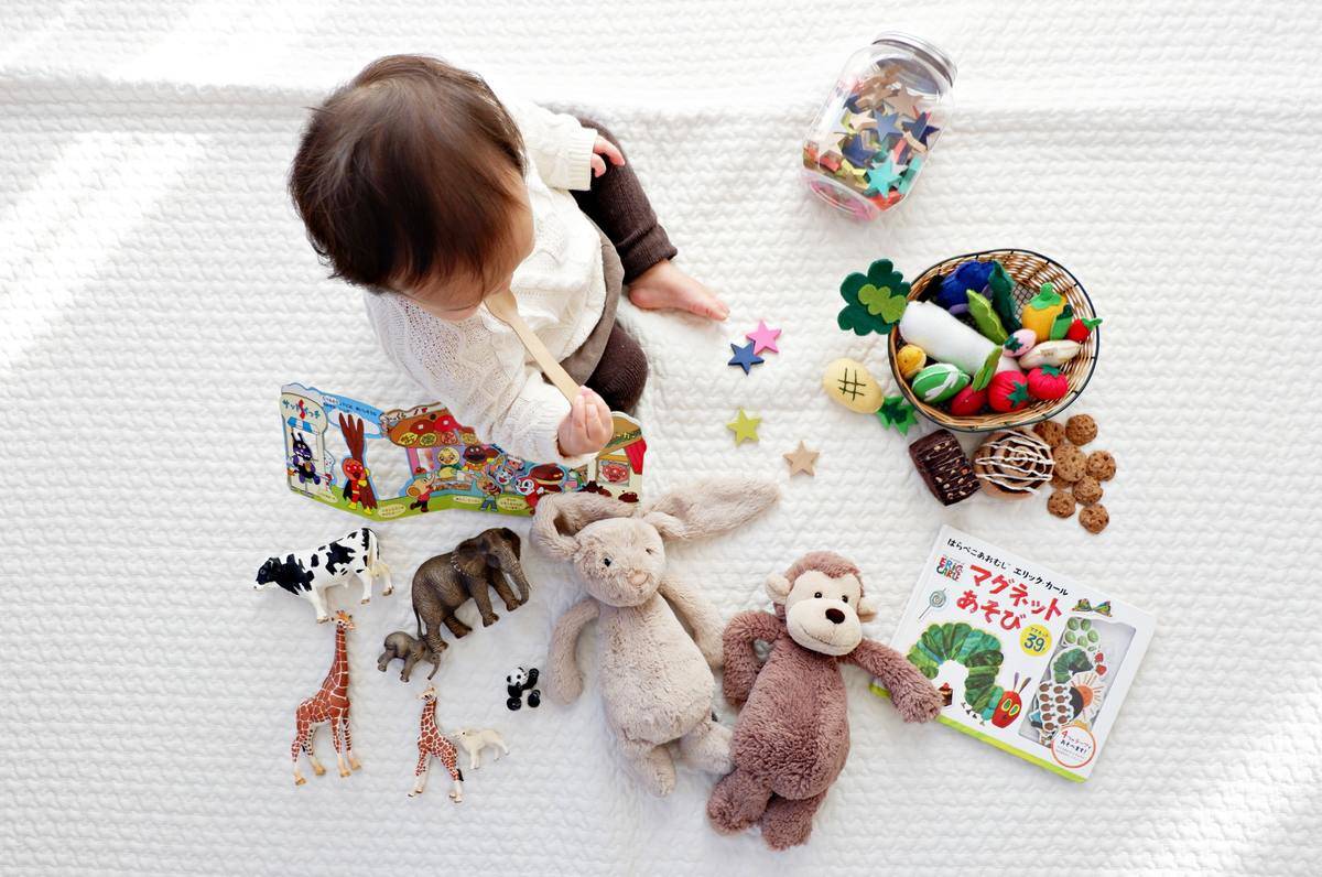 A baby sitting on a white mat with a bunch of toys laid out.