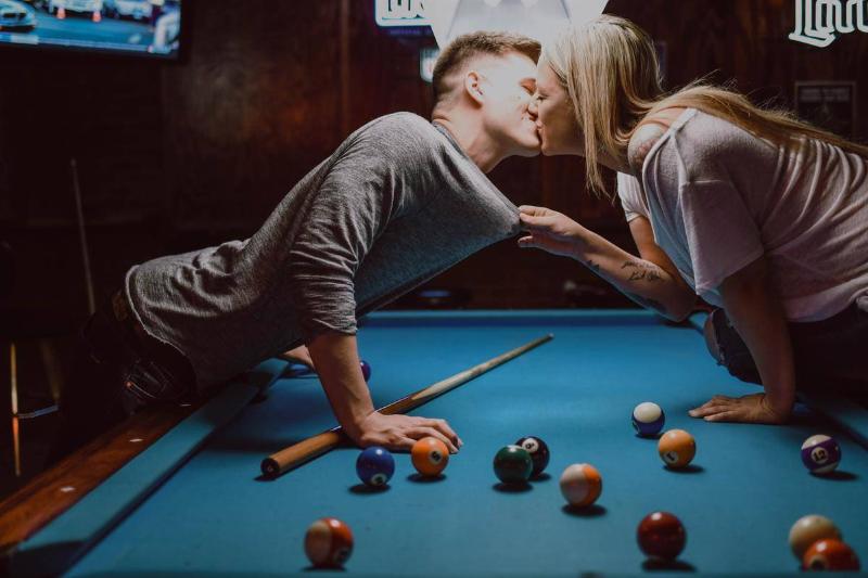 A man and woman kissing over a pool table.