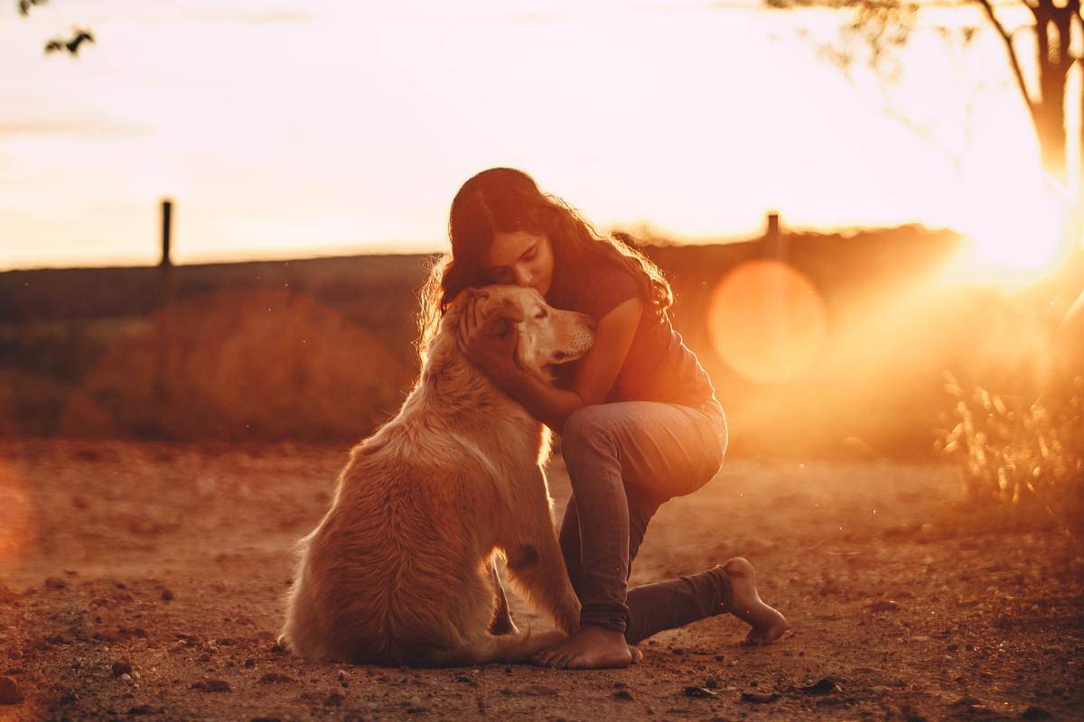 A young woman bent down, hugging her golden retriever at sunset.