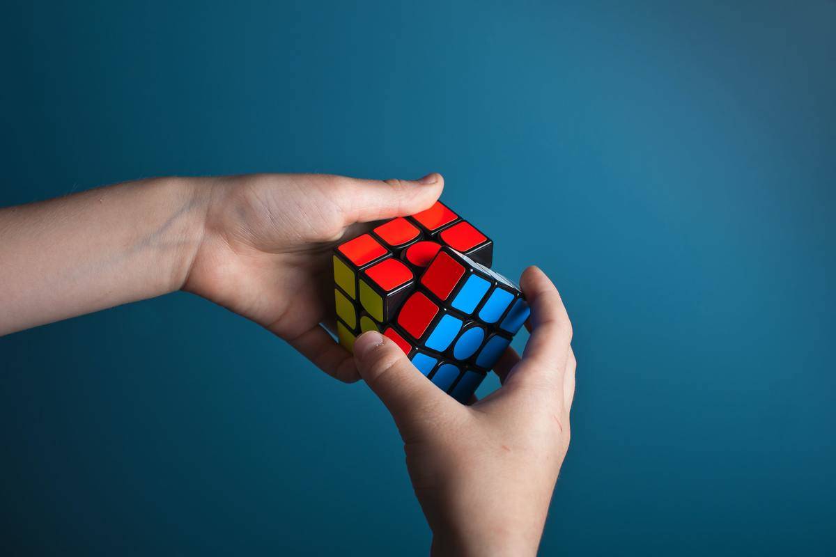Two hands holding a blue, red, and yellow Rubix cube.