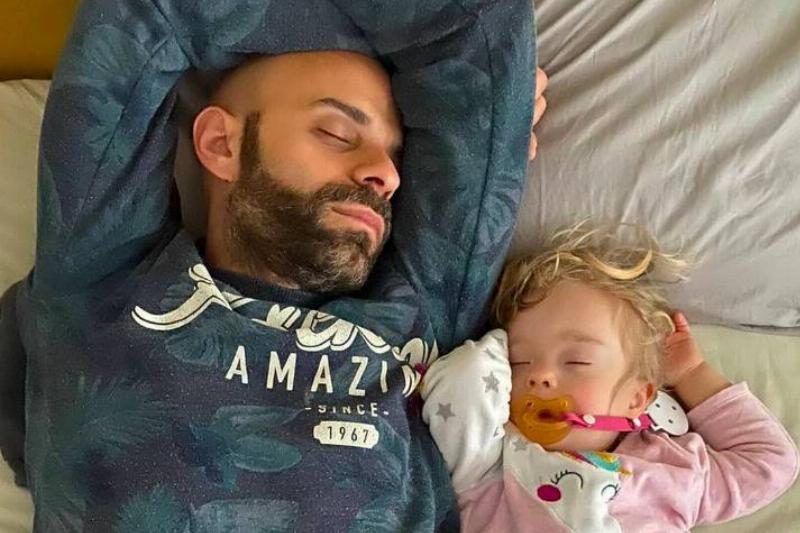 A father and baby girl sleeping side by side on a bed