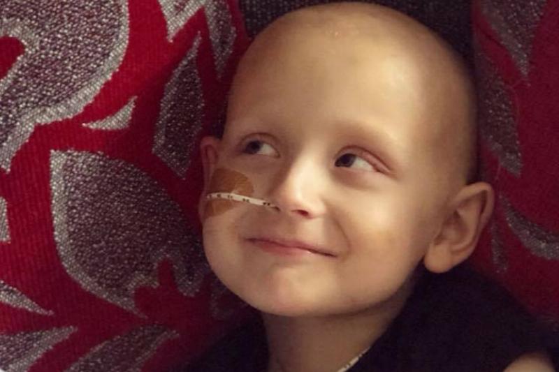 A young boy fighting cancer is smiling, with a tube in his nose.