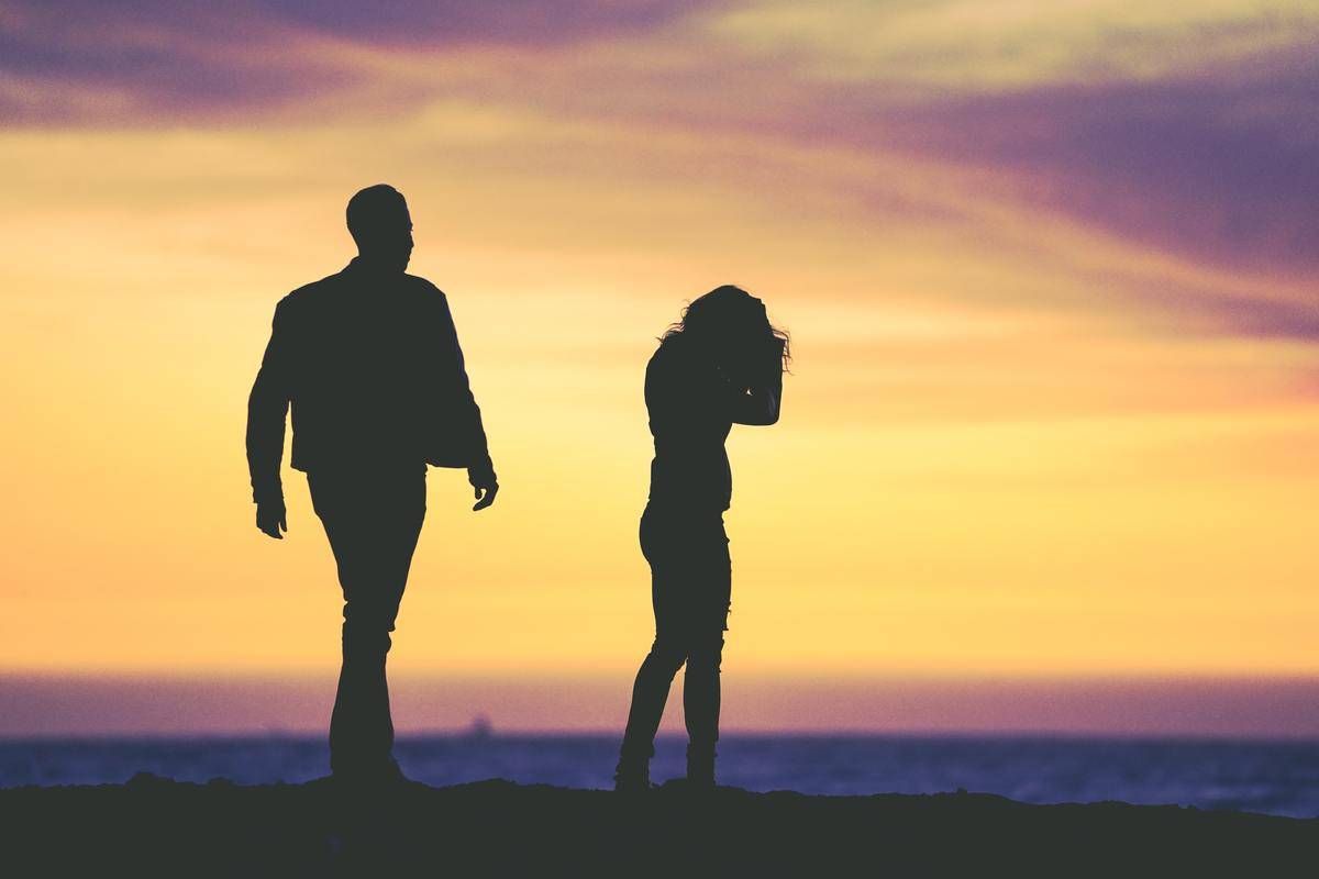 A silhouette of a man and woman turning away from each other at sunset.