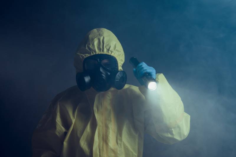 man in yellow hazmat suit and mask holds up flashlight