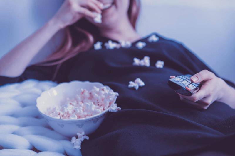 close up of woman holding tv remote wh while holding popcorn