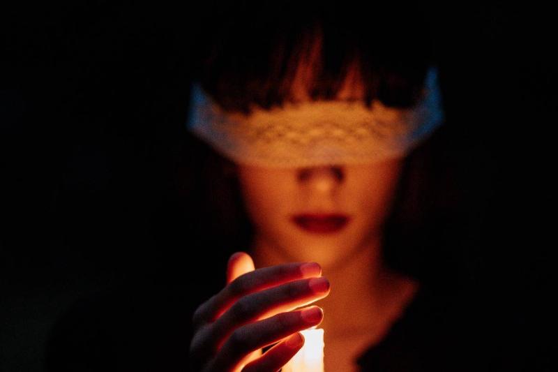 A female witch, blindfolded and holding a lit candle.