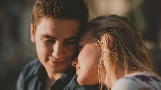 A young man and woman sitting, her head resting on his shoulders.