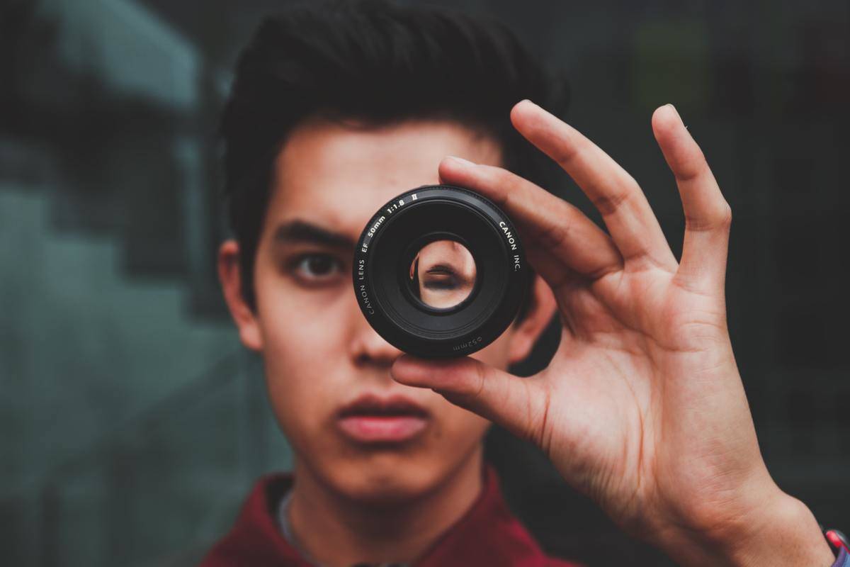 Young man looks through camera lens holding it to his eye