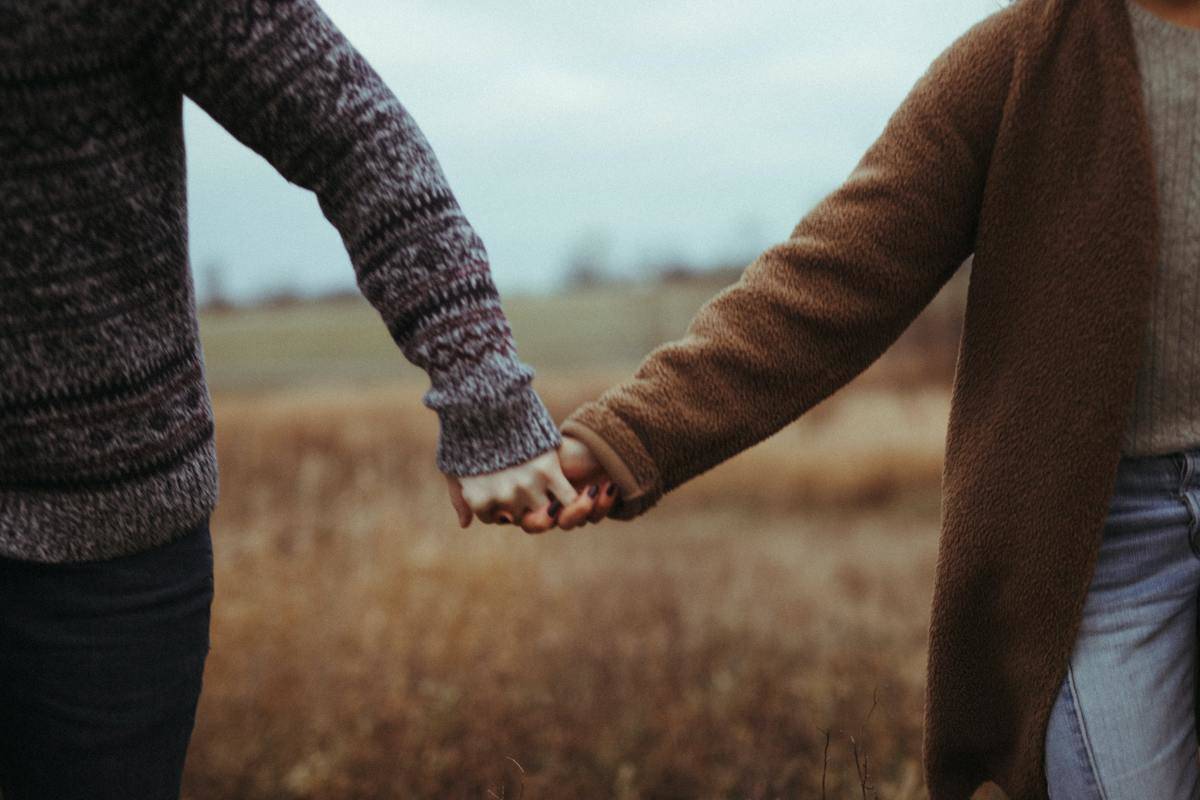 couple holding hands in a field with sweaters