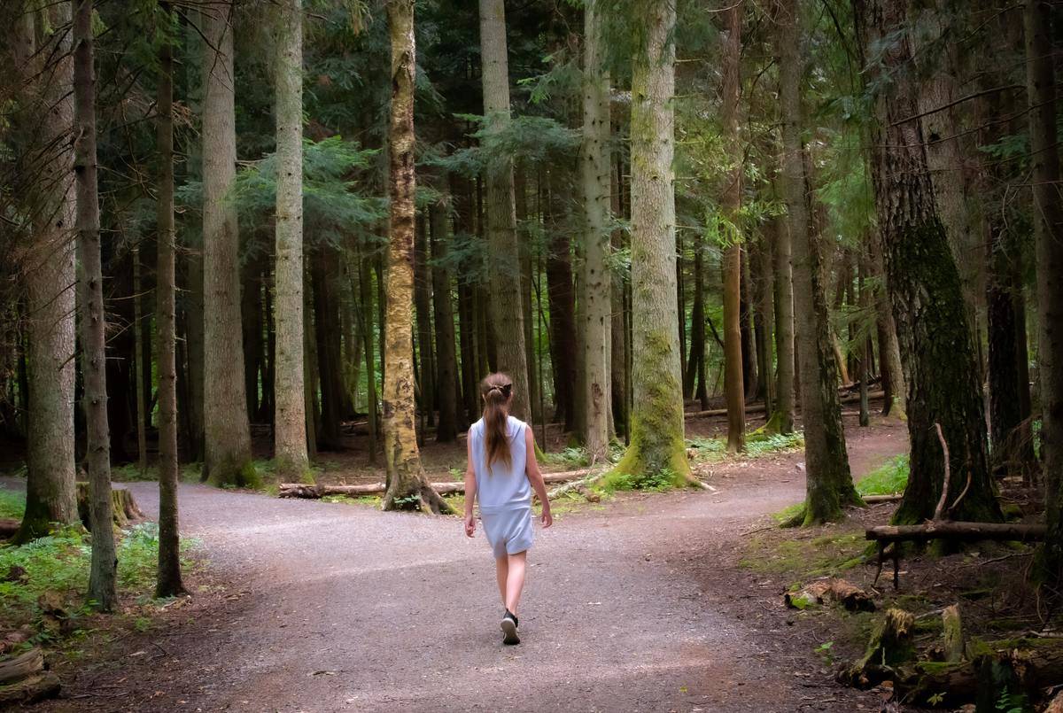 girl walking to the right of forest crossroad path