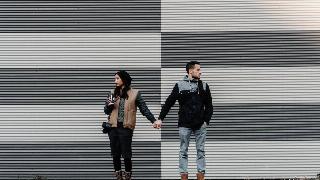 man and woman hold hands by black and white wall